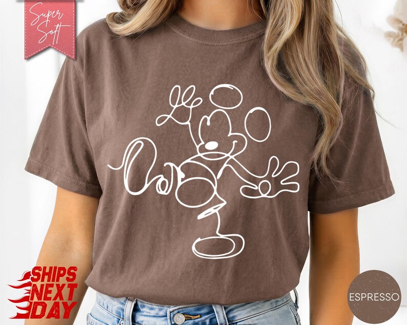 May include: Espresso-colored t-shirt featuring a white line drawing of Mickey Mouse with the word "Love" in cursive. The shirt has a relaxed fit and is made of soft material. The shirt has a vintage look.