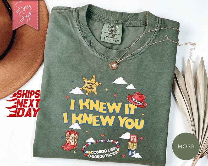 May include: A moss green short-sleeve t-shirt featuring a graphic print with the text I KNEW IT I KNEW YOU, a gold sheriff star badge with the text INFINITY AND BEYOND, a red cowboy hat, red cowboy boots, a beaded bracelet, and alphabet blocks.
