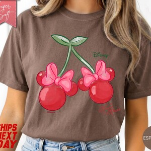 May include: Espresso-colored t-shirt featuring a whimsical design of cherries with pink bows, green leaves, and the Disney logo. The text "My Princess" is also visible. The shirt has a soft texture and is labeled "Super Soft".