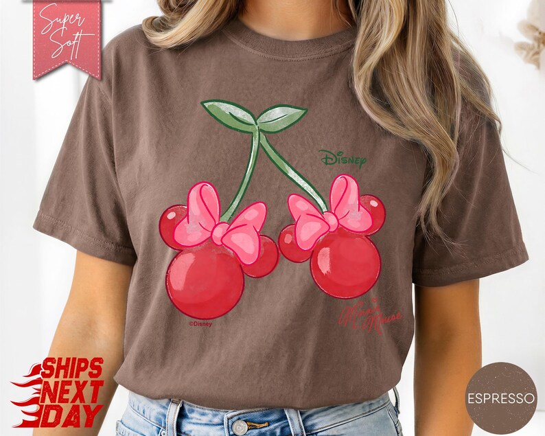 May include: Espresso-colored t-shirt featuring a whimsical design of cherries with pink bows, green leaves, and the Disney logo. The text "My Princess" is also visible. The shirt has a soft texture and is labeled "Super Soft".