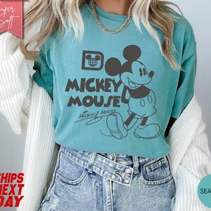 May include: Seafoam green t-shirt featuring a vintage Mickey Mouse graphic. The design includes the text "Mickey Mouse" and a drawing of Mickey. The shirt is a soft, casual style.