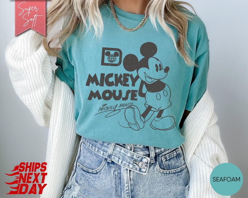 May include: Seafoam green t-shirt featuring a vintage Mickey Mouse graphic. The design includes the text "Mickey Mouse" and a drawing of Mickey. The shirt is a soft, casual style.