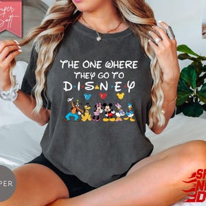K&ouml;nnte beinhalten: Dunkelgraues T-Shirt mit dem Text "THE ONE WHERE THEY GO TO DISNEY" und Disney-Figuren. Das Shirt hat einen Rundhalsausschnitt und kurze &Auml;rmel. Das Design umfasst Micky Maus, Minnie Maus, Donald Duck und Goofy.