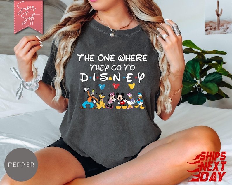 K&ouml;nnte beinhalten: Dunkelgraues T-Shirt mit dem Text "THE ONE WHERE THEY GO TO DISNEY" und Disney-Figuren. Das Shirt hat einen Rundhalsausschnitt und kurze &Auml;rmel. Das Design umfasst Micky Maus, Minnie Maus, Donald Duck und Goofy.