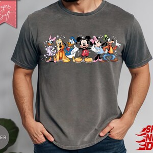 Puede incluir: Una camiseta gris carb&oacute;n con un gr&aacute;fico colorido de personajes de Disney, incluyendo a Daisy, Pluto, Donald, Mickey, Minnie y Goofy. La camiseta tiene el texto "Super Soft" en una pancarta rosa.