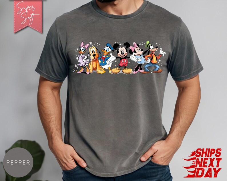 Puede incluir: Una camiseta gris carb&oacute;n con un gr&aacute;fico colorido de personajes de Disney, incluyendo a Daisy, Pluto, Donald, Mickey, Minnie y Goofy. La camiseta tiene el texto "Super Soft" en una pancarta rosa.