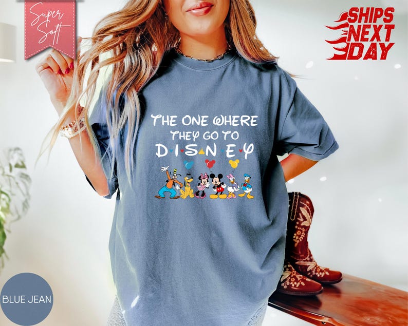 K&ouml;nnte beinhalten: Blaues Jeans-T-Shirt mit dem Text "The One Where They Go To Disney" und Disney-Figuren. Das Shirt hat einen Rundhalsausschnitt und kurze &Auml;rmel. Die Worte "Super Soft" stehen in einem rosa Banner.