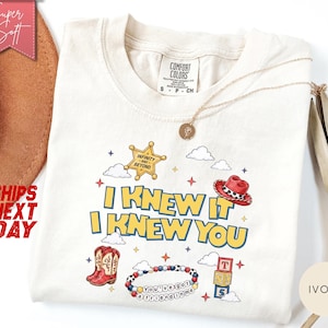 May include: An ivory t-shirt featuring a graphic print with the text I KNEW IT I KNEW YOU, a yellow sheriff star with the text INFINITY AND BEYOND, a red cowboy hat, red cowboy boots, a beaded bracelet with the text YOU'VE GOT A FRIEND IN ME, and blocks.
