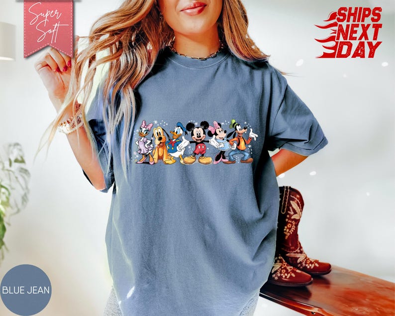 Puede incluir: Camiseta de color azul vaquero con un gr&aacute;fico colorido de personajes de Disney. El gr&aacute;fico incluye Mickey y Minnie Mouse, el Pato Donald, Goofy, Daisy Duck y Pluto. La camiseta tiene las palabras "Super Soft" y "Ships Next Day".