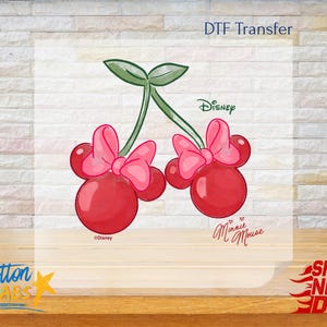 May include: DTF Transfer featuring a pair of red cherries with pink bows, designed in the style of Minnie Mouse. The image includes the Disney logo and the words "Minnie Mouse".