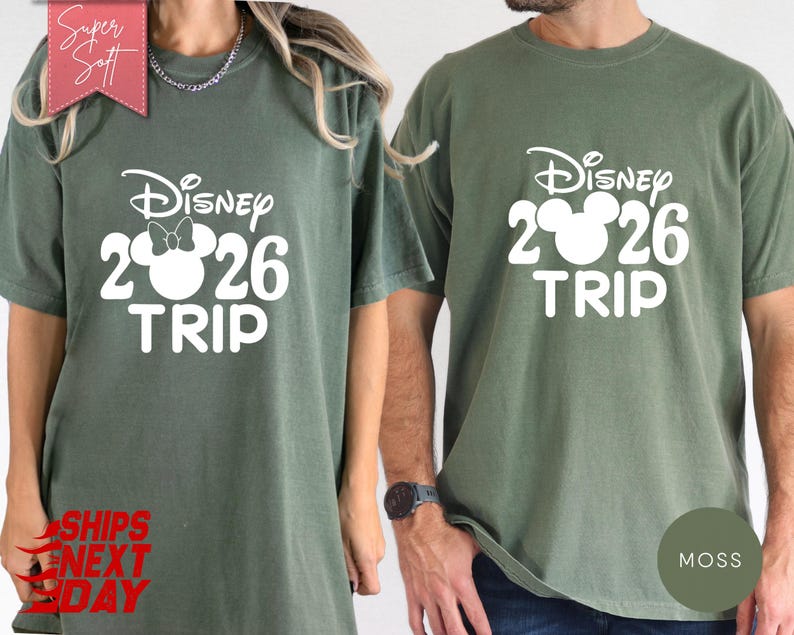 May include: Two olive green t-shirts with the text "Disney 2026 TRIP" in white. One shirt features a Minnie Mouse design. The shirts have short sleeves and a crew neck. The words "Super Soft" and "Ships Next Day" are also visible.