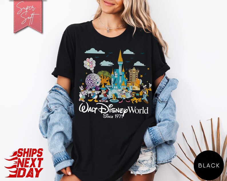 K&ouml;nnte beinhalten: Schwarzes T-Shirt mit einer farbenfrohen Grafik des Walt Disney World Schlosses, Figuren und der EPCOT-Kugel. Der Text "Walt Disney World Since 1971" ist darunter gedruckt. Das T-Shirt hat kurze &Auml;rmel.