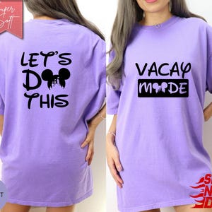 May include: A violet-colored t-shirt with the text "LET'S DO THIS" and a Mickey Mouse silhouette on the back. The front of the shirt features the words "VACAY MODE" with a Mickey Mouse silhouette. The shirt is a casual, oversized fit.