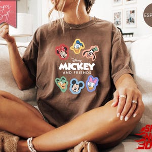 May include: Espresso-colored t-shirt featuring the text "Mickey and Friends" with colorful character graphics. The shirt has a relaxed fit and is made of soft material. The shirt is a comfortable and stylish choice for fans of the classic Disney characters.