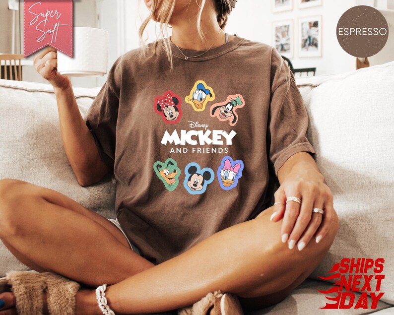 May include: Espresso-colored t-shirt featuring the text "Mickey and Friends" with colorful character graphics. The shirt has a relaxed fit and is made of soft material. The shirt is a comfortable and stylish choice for fans of the classic Disney characters.