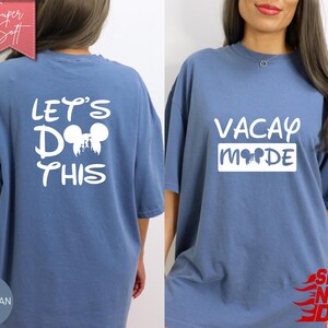May include: Blue jean-colored t-shirt with white text and graphics. The front of the shirt says "VACAY MODE" with a Mickey Mouse head silhouette. The back says "LET'S DO THIS" with a Mickey Mouse head and castle graphic.