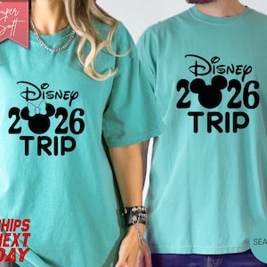 May include: Two teal-colored t-shirts with the text "Disney 2026 TRIP" in black. One shirt has a Minnie Mouse bow graphic, the other has a Mickey Mouse graphic. The shirts are made of a soft material.
