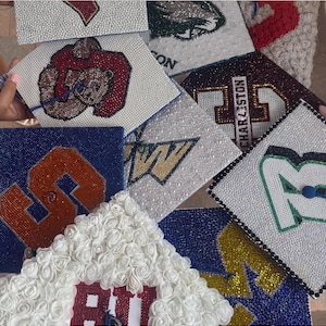 Peut inclure: Plusieurs coiffes de graduation décorées. Les coiffes présentent divers motifs, notamment des logos d'écoles, des initiales et le mot "Charleston". Les embellissements comprennent des strass, des perles et des accents floraux. Les couleurs incluent le bleu, l'orange, le blanc et le vert.