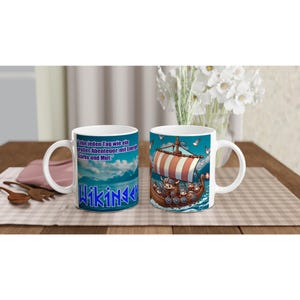 Può includere: Tazza in ceramica bianca con un design di nave vichinga dei cartoni animati e una vela a strisce rosse e bianche. La tazza ha uno sfondo blu con la parola "WIKINGER" in testo blu e bianco. La tazza ha anche testo tedesco.