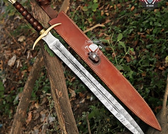 May include: A detailed image of a sword with a patterned blade, gold-colored crossguard, and a brown handle. The sword rests beside a brown leather sheath. The handle has a dark brown grip. The background is a natural setting with wood and foliage.