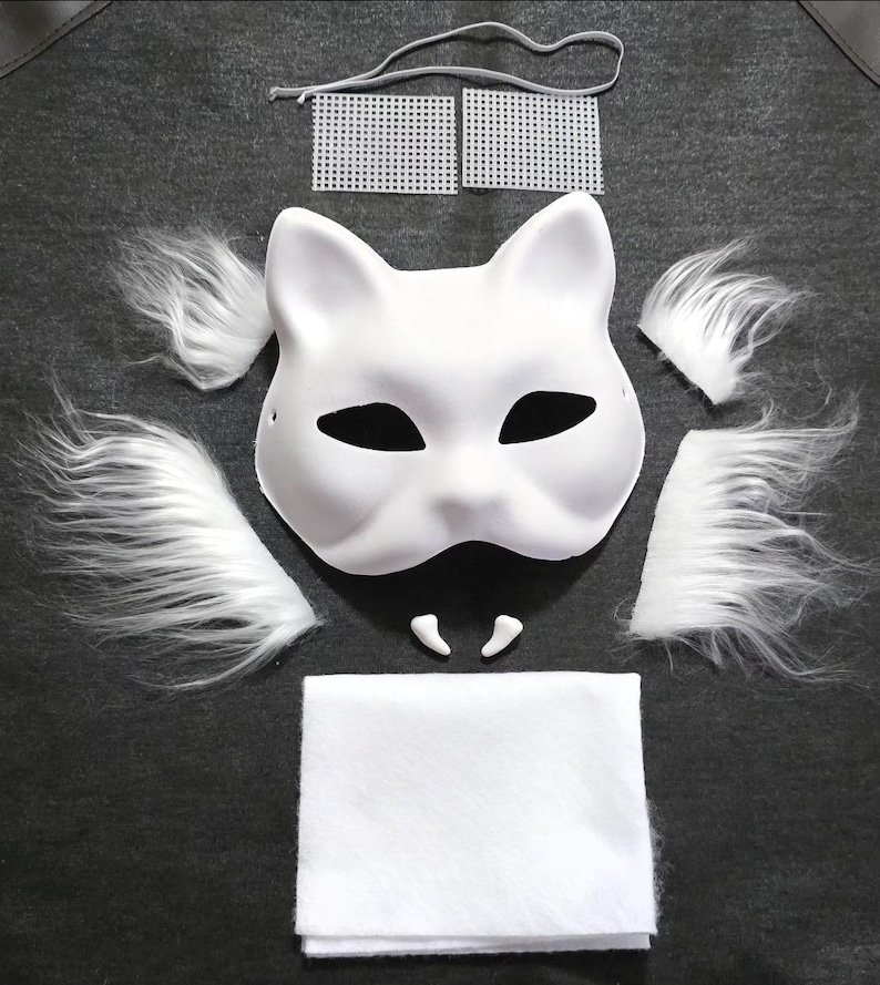 Op de afbeelding: Een wit kattenmasker met zwarte ooguitsparingen, vergezeld van witte imitatiebontstukken, tanden en een wit vilten vierkant. Inclusief een grijs elastisch koord en twee witte plastic gaasvierkanten. Ideaal voor kostuum- of knutselprojecten.