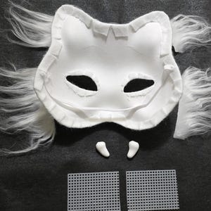 May include: A white animal-shaped mask base with attached long white faux fur tufts on the sides. The mask features two eye openings, two small white tooth-like attachments positioned below the mask, and two separate white plastic mesh squares.