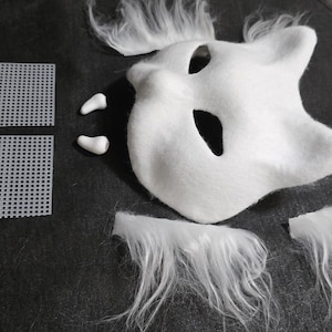 May include: A white animal-shaped mask with pointed ears and eye cutouts, accompanied by two small white fangs, two square pieces of white plastic mesh, and four separate tufts of long white faux fur for assembly or decorative customization.