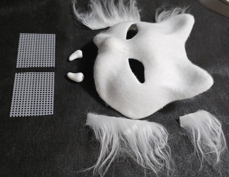 May include: A white animal-shaped mask with pointed ears and eye cutouts, accompanied by two small white fangs, two square pieces of white plastic mesh, and four separate tufts of long white faux fur for assembly or decorative customization.