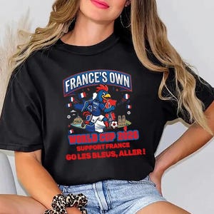 A woman wearing a black t-shirt with a graphic design featuring a cartoon rooster and text promoting France's participation in the World Cup.