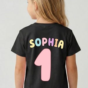 A young girl wearing a black t-shirt with the name "Sophia" and the number "1" printed on it.