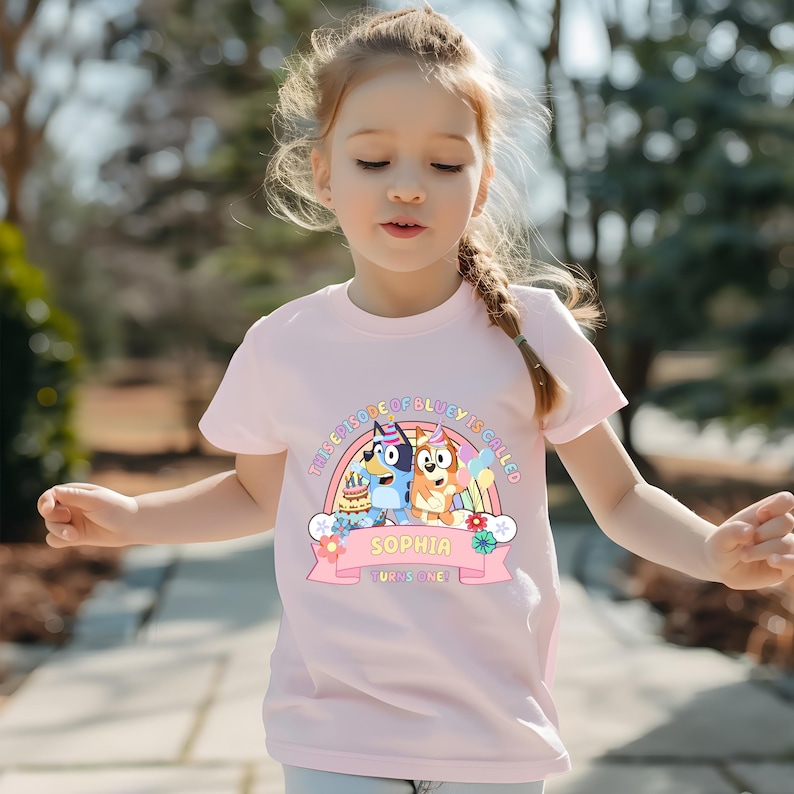 A young girl wearing a pink t-shirt with a cartoon character design and text on it.