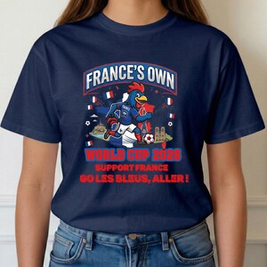 A blue t-shirt with a graphic design featuring a cartoon rooster and various French-themed elements, along with text promoting the French national team's participation in the World Cup.