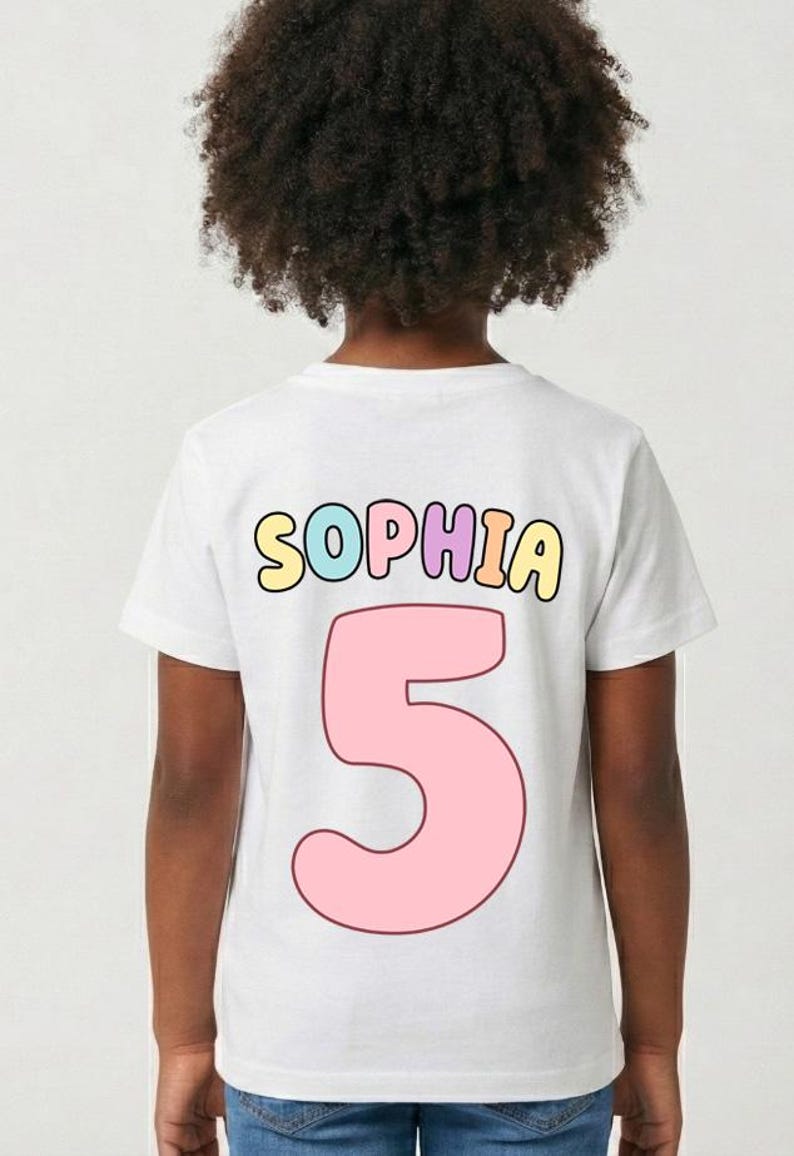 A child with curly hair wearing a white t-shirt with the name "Sophia" and the number "5" printed on it.