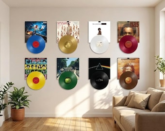 May include: A collection of framed album covers with vinyl records in various colors, including blue, gold, white, red, yellow, green, black, and brown. The records are mounted on a white wall, creating a music-themed display.