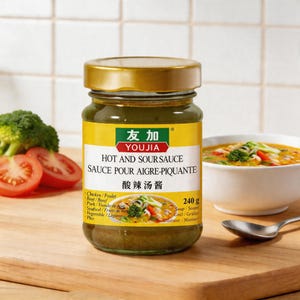May include: A jar of Youjia Hot and Sour Sauce with a gold lid and a yellow label. The label includes text in English, French, and Chinese. Broccoli and sliced tomatoes are visible to the left, and a bowl of soup is on the right.