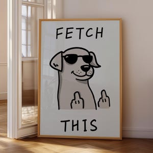 Könnte beinhalten: Ein gerahmter Druck mit einem Cartoon-Hund, der eine Sonnenbrille trägt und den Mittelfinger zeigt. Die Worte "FETCH THIS" sind oberhalb und unterhalb der Hundeillustration in fetten, schwarzen Buchstaben gedruckt. Das Kunstwerk wird in einem Raum mit Holzboden ausgestellt.