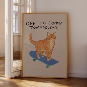 Może przedstawiać: Oprawiony wydruk przedstawiający pomarańczowego kota pręgowanego na niebieskiej deskorolce. Wydruk zawiera tekst "OFF TO COMMIT TOMFOOLERY". Kot ma zielone oczy. Rama jest drewniana.