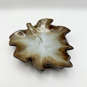 May include: A decorative leaf-shaped dish with a glossy finish. The dish features a blend of brown and white colors, creating a marbled effect. The edges are dark brown, and the interior has a lighter, swirling pattern.