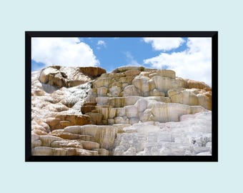 Könnte beinhalten: Gerahmtes Foto einer Naturlandschaft. Das Bild zeigt eine geschichtete Felsformation in Weiß-, Beige- und Brauntönen. Ein blauer Himmel mit flauschigen weißen Wolken ist im Hintergrund zu sehen. Das Foto ist in einem schwarzen Rahmen eingefasst.