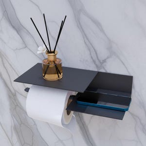 May include: A modern, wall-mounted toilet paper holder with a built-in shelf. The holder is dark gray and features a shelf for a phone and a small bottle of fragrance with reeds. The design is sleek and minimalist, perfect for a contemporary bathroom.