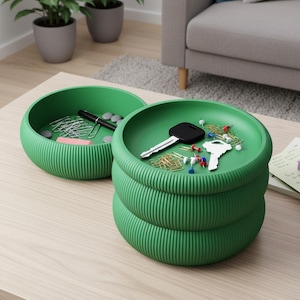 Puede incluir: Dos bandejas redondas verdes y acanaladas sobre una mesa de madera clara. Una bandeja contiene clips, un bolígrafo y gomas de borrar. La otra bandeja contiene llaves, chinchetas y clips. Las bandejas están junto a un cuaderno y un sofá.