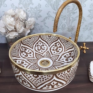 May include: A round ceramic vessel sink featuring a brown and white intricate floral pattern with a gold-toned rim. The sink includes a tall, curved, gold-toned metal tap with a textured surface and a matching gold-toned drain assembly.