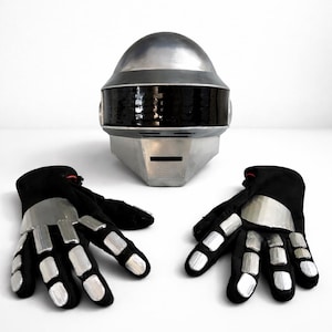 Może przedstawiać: Srebrny i czarny hełm robota z czarnym wizjerem i srebrną osłoną czołową. Dwie czarne rękawice ze srebrnymi płytkami na palce i nadgarstki znajdują się przed hełmem. Zestaw jest prawdopodobnie przeznaczony na kostium lub cosplay.