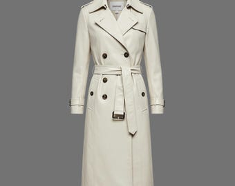 May include: A cream-colored trench coat with a double-breasted design. The coat features a belt, notched lapels, and button details. The coat is a long length, reaching the ankles.