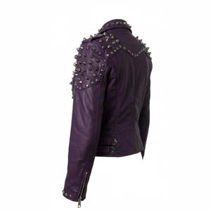 May include: A purple leather jacket with silver metal cone studs on the shoulders and collar. The jacket has a zipper closure on the front and sleeves, and two buckle straps at the waist. The jacket is a classic biker style.