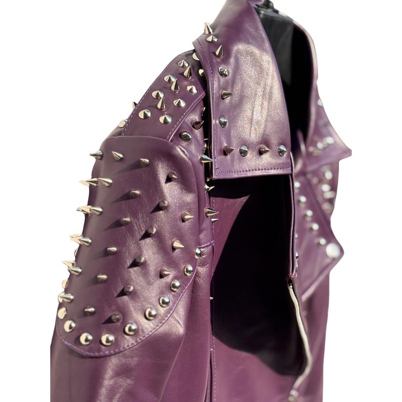 May include: A purple leather jacket with silver metal spikes on the shoulders, collar, and upper sleeves. The jacket has a classic biker style with a notched lapel and a zipper closure. The jacket is displayed on a black mannequin.