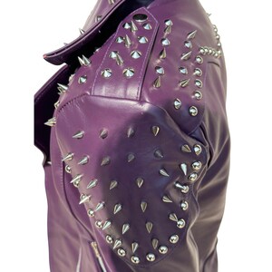 May include: A close-up of a purple leather jacket with silver cone-shaped studs on the shoulders and upper sleeves. The jacket has a notched collar and a zipper. The leather has a slight sheen.