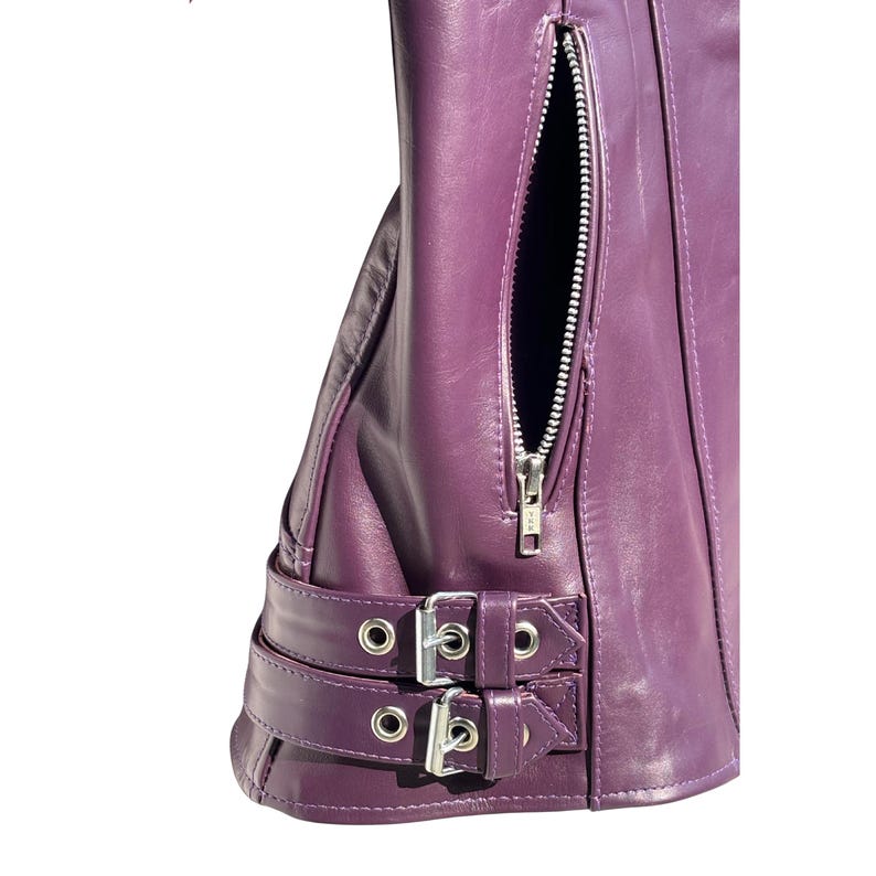 May include: Close-up of a purple leather jacket with a silver zipper and buckle details. The jacket features a vertical zippered pocket and two adjustable straps with silver buckles. The leather has a smooth texture.