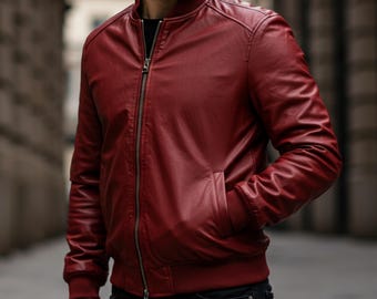 May include: A burgundy leather bomber jacket with a ribbed collar, cuffs, and hem. The jacket features a front zipper closure and two side pockets. The model is wearing a black shirt and black jeans.
