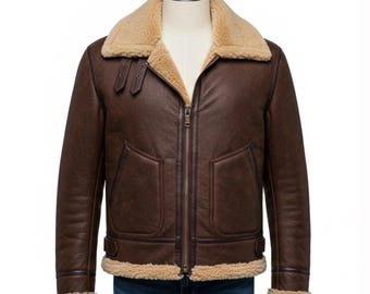 May include: A brown leather jacket with a shearling collar and lining. The jacket features a zip-up front, two front pockets, and buckle details. The jacket is displayed on a mannequin.